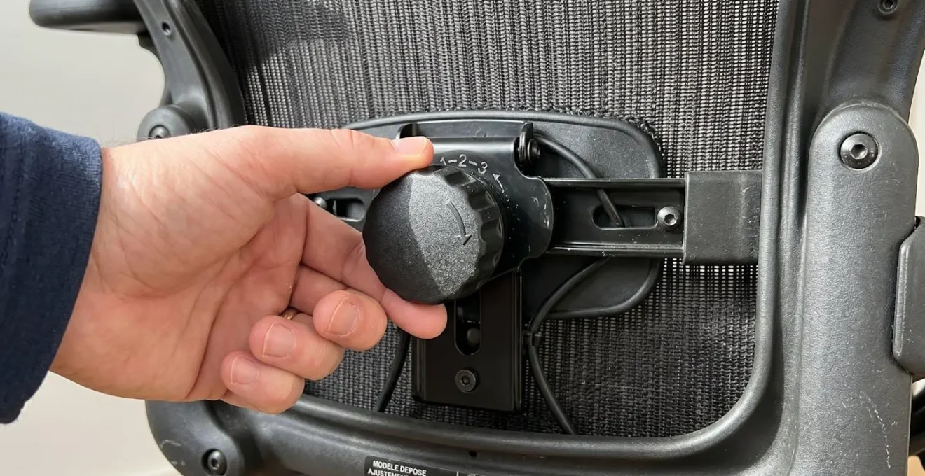 Gros plan sur la molette de réglage du soutien lombaire d'une chaise ergonomique avec tissu maille visible en arrière-plan flouté